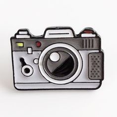 a black and white photo camera pin on a white surface with the lens pointed up