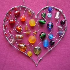 a heart shaped metal decoration with lots of different colored glass beads hanging from it's sides