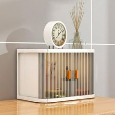 a clock sitting on top of a white cabinet next to a vase and reeds