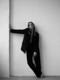 a woman leaning against a wall wearing a suit