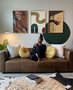 a woman sitting on a couch in front of some paintings and drinking a glass of wine