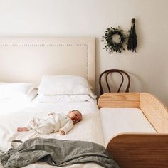 a baby laying on top of a white bed next to a wooden dresser and chair