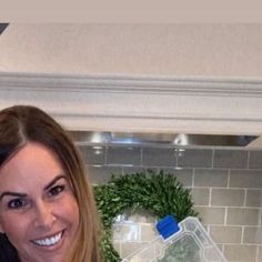 a woman standing in front of a stove top oven holding a glass container filled with herbs