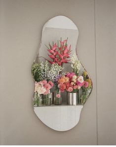 a mirror that has flowers in it on the wall next to a shelf with vases