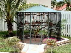 a bird cage sitting on top of a lush green field next to a white fence