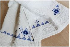 two white towels with blue flowers on them sitting on a wooden table next to each other