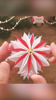 a person holding a paper flower in their hand with beads on the table next to it