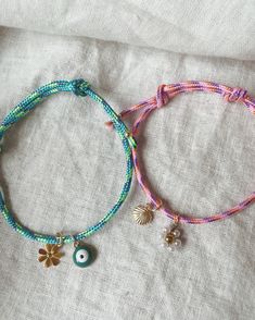 two bracelets with charms are laying on a bed