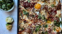 an egg and cheese pizza on a baking sheet next to a bowl of salad greens