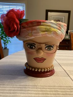 a close up of a vase on a table with a plant in the middle and a face painted on it