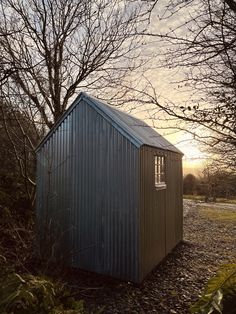 a small metal building sitting in the middle of a field next to some bare trees