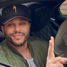 a man sitting in the driver's seat of a car with his hand up