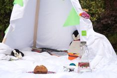 there is a stuffed penguin sitting in front of a teepee tent with food and drinks on it