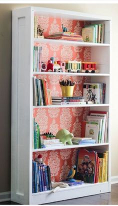 a bookshelf filled with lots of books next to a wallpapered wall