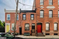 an old brick building with red door and black car parked on the street in front