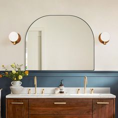 a bathroom vanity with two sinks and a large round mirror above it, against a blue wall