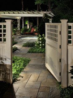 an open gate leading into a garden at night with lights on the top and bottom