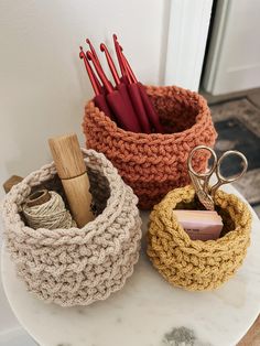 three crocheted baskets sitting on top of a marble table with scissors and yarn