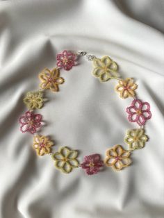 a close up of a bracelet on a white cloth with pink, yellow and green flowers