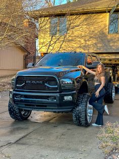 a woman standing next to a large black truck in front of a house with her hand on the hood