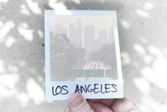 a person holding up a polaroid with the word los angeles written on it in front of them