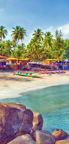 there are many boats that are on the water by the beach and some rocks in front of them