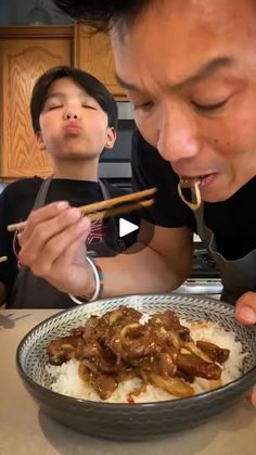 a man eating food with chopsticks in front of him and another person looking on