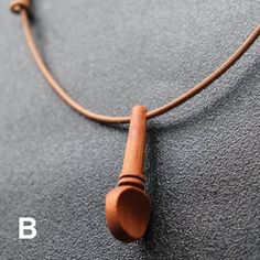 a necklace with a wooden tube hanging from it's side on a gray surface