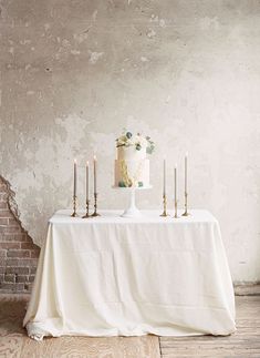 a table topped with a white cake and three candles next to a brick wall in an old room