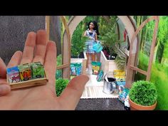 a hand is holding a miniature doll in front of a fake garden area with potted plants