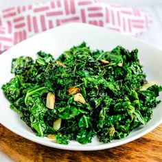 a white bowl filled with green vegetables on top of a wooden cutting board next to a red and white towel