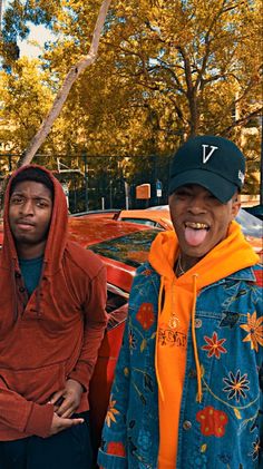 two men standing next to each other in front of parked cars