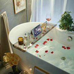 a bathtub with rose petals on the floor next to a glass of wine and candles