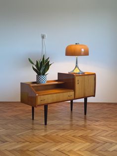 a wooden table with a plant on it and a lamp next to it in the corner