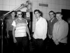 a group of men standing next to each other in front of a microphone and recording equipment