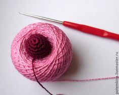 a ball of pink yarn next to a crochet hook and red handled knitting needle