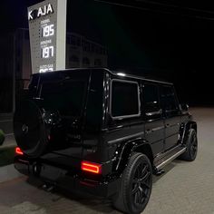 a black mercedes g - class is parked in front of a gas station at night