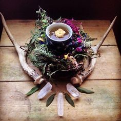 an arrangement of antlers and flowers on top of a wooden table, with a cup in the center