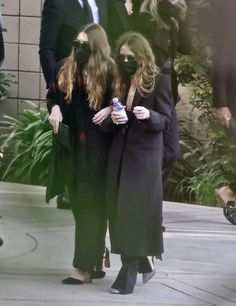 two women wearing masks are walking down the street while another woman is holding a cell phone