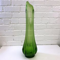 a green glass vase sitting on top of a white table next to a brick wall