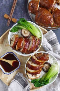 two bowls filled with meat and vegetables on top of a wooden tray next to chopsticks