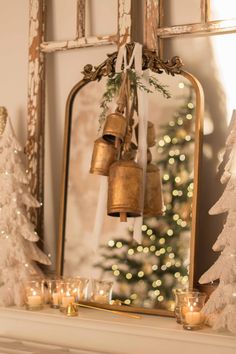 a mantel with candles, christmas trees and bells on it in front of a mirror