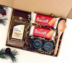 an open box with coffee, cookies and spoons in it next to pine cones