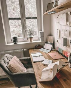 a desk with two laptops and books on it in front of a large window