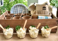 four small cups filled with food sitting on top of a wooden tray next to plants