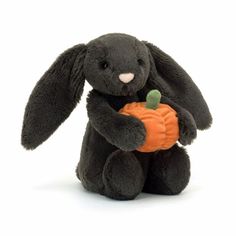 a black stuffed rabbit holding a pumpkin