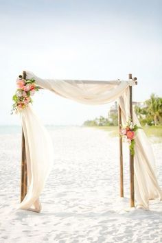 an outdoor wedding setup on the beach with white draping and pink flowers at the top