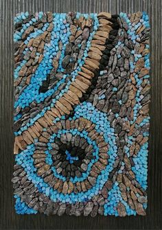 a piece of art made out of rocks and pebbles on a wooden surface with a circular design in the middle