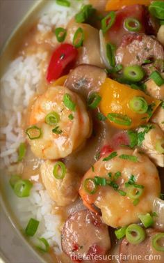 a white plate topped with rice and shrimp covered in sauce, green onions and peppers