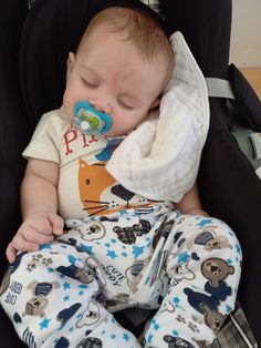 a baby sleeping in a car seat with a pacifier in his mouth and wearing pajamas